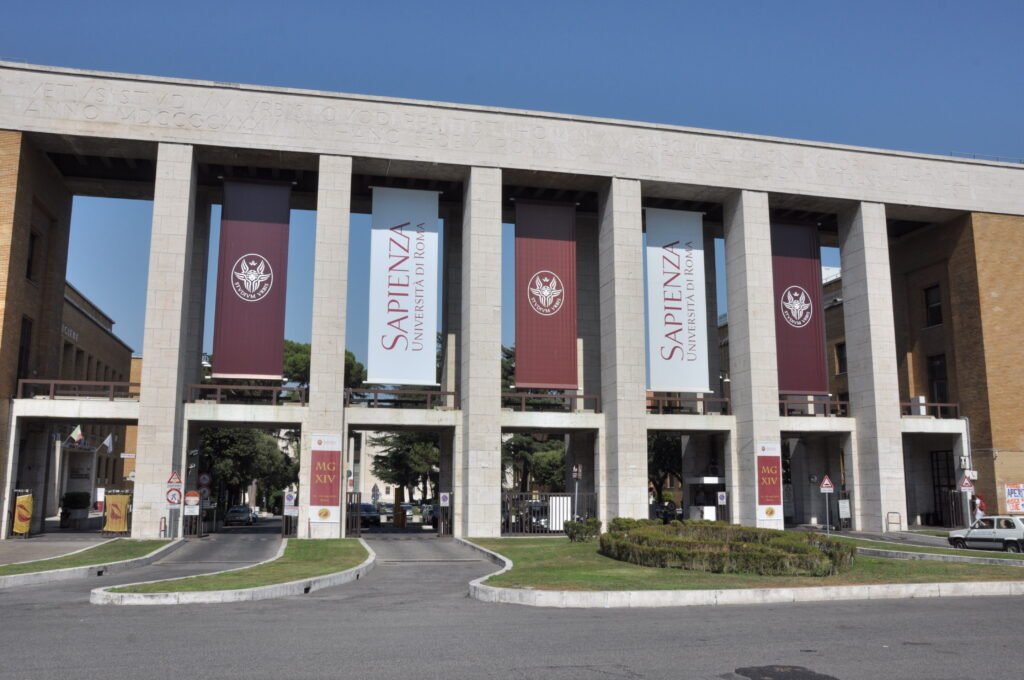 Sapienza Università di Roma’nın mavi gökyüzü önündeki sütunlu ana girişi ve üniversite flamaları